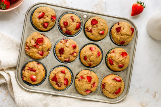 Twelve strawberry yogurt muffins wrapped in silicone liners in a muffin tin.