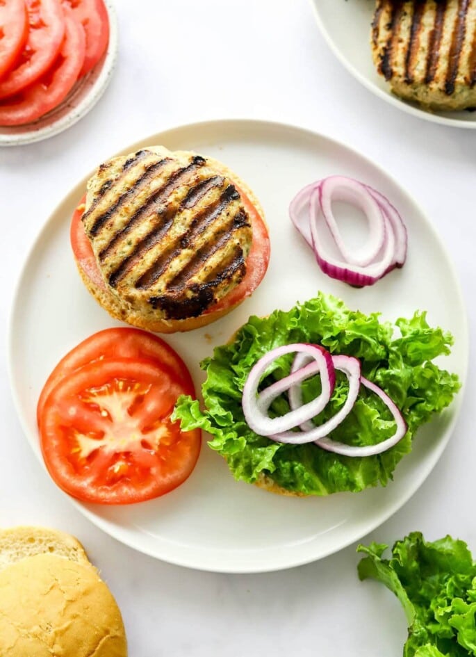 An open faced turkey burger on a plate with tomato, red onion and lettuce.