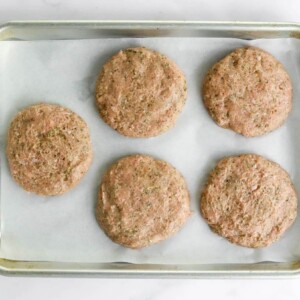 5 uncooked turkey burger patties on a sheet pan lined with parchment paper.