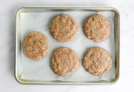 5 uncooked turkey burger patties on a sheet pan lined with parchment paper.