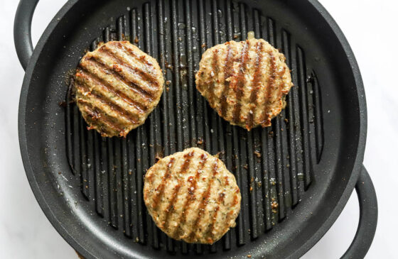 Three turkey burgers cooking on a grill.