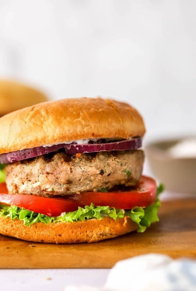 A turkey burger on a bun with lettuce, tomato and red onion.