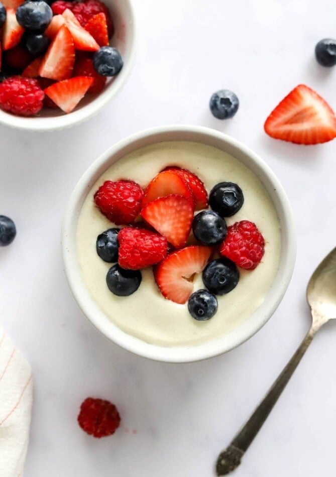 A small dish containing vanilla protein pudding topped with berries.