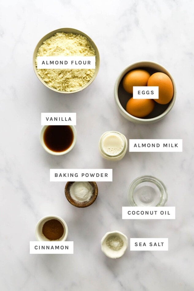 Ingredients measured out to make almond flour waffles: almond flour, eggs, vanilla, almond milk, baking powder, coconut oil, cinnamon and sea salt.