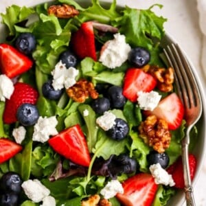 Bowl with a salad topped with maple walnuts, blueberries, goat cheese and strawberries.