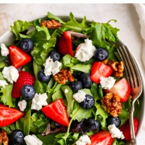 Bowl with a salad topped with maple walnuts, blueberries, goat cheese and strawberries.