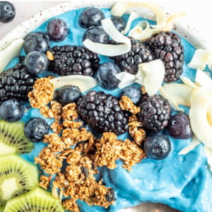 Overhead photo of a blue majik smoothie bowl topped with kiwi, granola, blackberries, blueberries and coconut flakes.