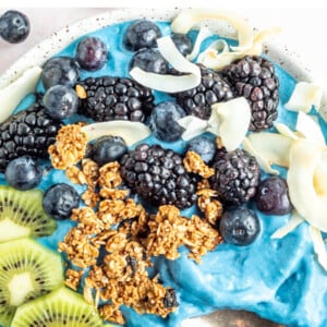Overhead photo of a blue majik smoothie bowl topped with kiwi, granola, blackberries, blueberries and coconut flakes.