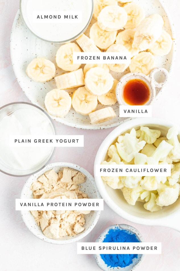 Ingredients measured out to make a blue smoothie bowl: almond milk, frozen banana, vanilla, plain Greek yogurt, frozen cauliflower, vanilla protein powder and blue spirulina powder.