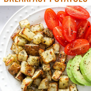 An overhead view of a plate containing air fryer breakfast potatoes alongside tomato and avocado slices.