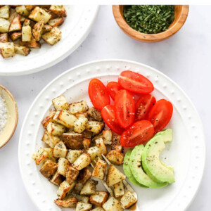 An overhead view of a plate containing air fryer breakfast potatoes alongside tomato and avocado slices.