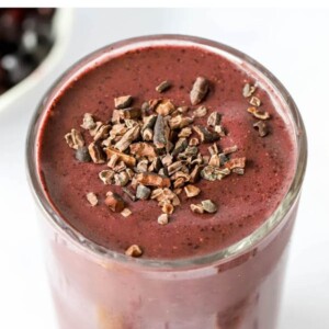 A glass cup filled with cacao smoothie topped with cacao shavings.