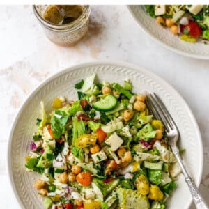 Overhead view of a plate containing Italian chopped salad. A jar containing dressing is resting next to the plate.