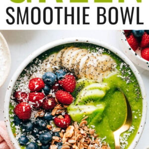 A green smoothie bowl topped with granola, shredded coconut, berries, banana and kiwi. A spoon rests in the bowl.