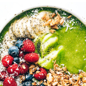 A green smoothie bowl topped with granola, shredded coconut, berries, banana and kiwi.