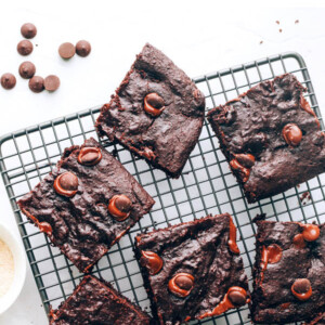 Overhead view of a wire cooling rack with lactation brownies scattered around. A hand is grabbing a brownie from the bottom.