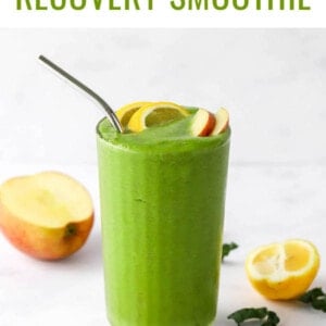 A drinking glass filled with recovery smoothie, topped with lemon and apple wedges. A metal straw sticks out of the top.