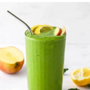 A drinking glass filled with recovery smoothie, topped with lemon and apple wedges. A metal straw sticks out of the top.