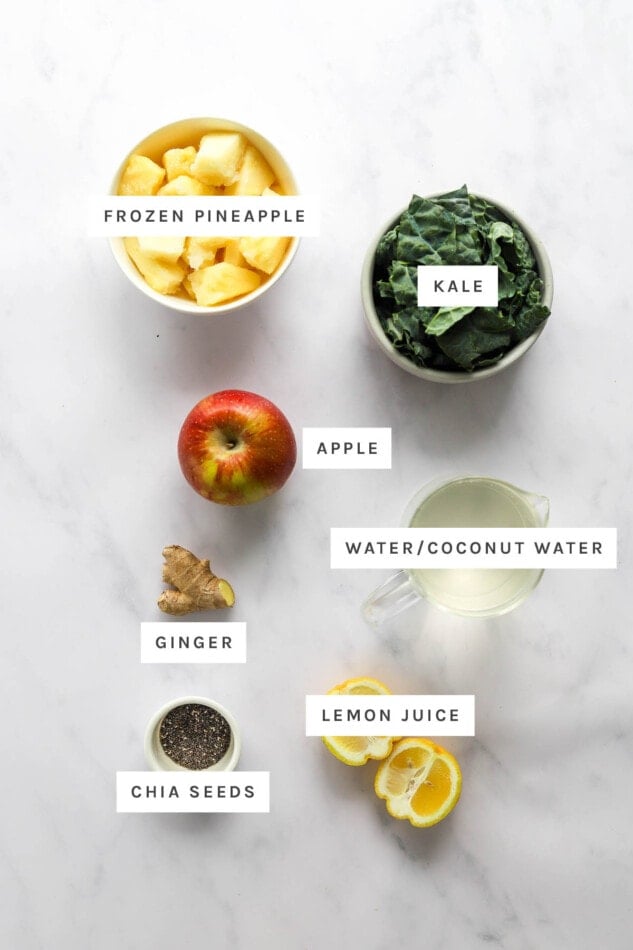 Ingredients measured out to make a Pineapple Recovery Smoothie: frozen pineapple, kale, apple, water/coconut water, ginger, lemon juice and chia seeds.