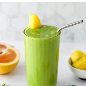 A glass containing vitamin c smoothie. It's topped with a wedge of pineapple and a straw.