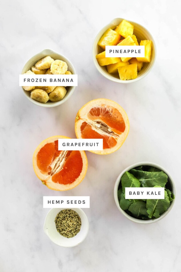 Ingredients measured out out to make a vitamin c smoothie: pineapple, frozen banana, grapefruit, baby kale and hemp seeds.