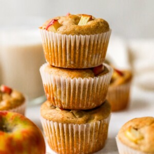 Three apple yogurt muffins stacked on top of each other. The muffins are wrapped in paper liners.