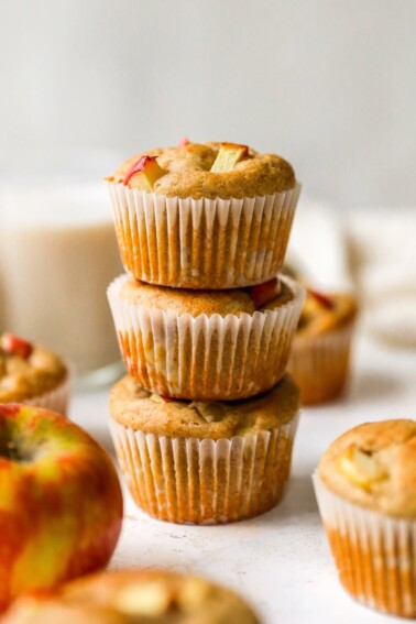 Three apple yogurt muffins stacked on top of each other. The muffins are wrapped in paper liners.