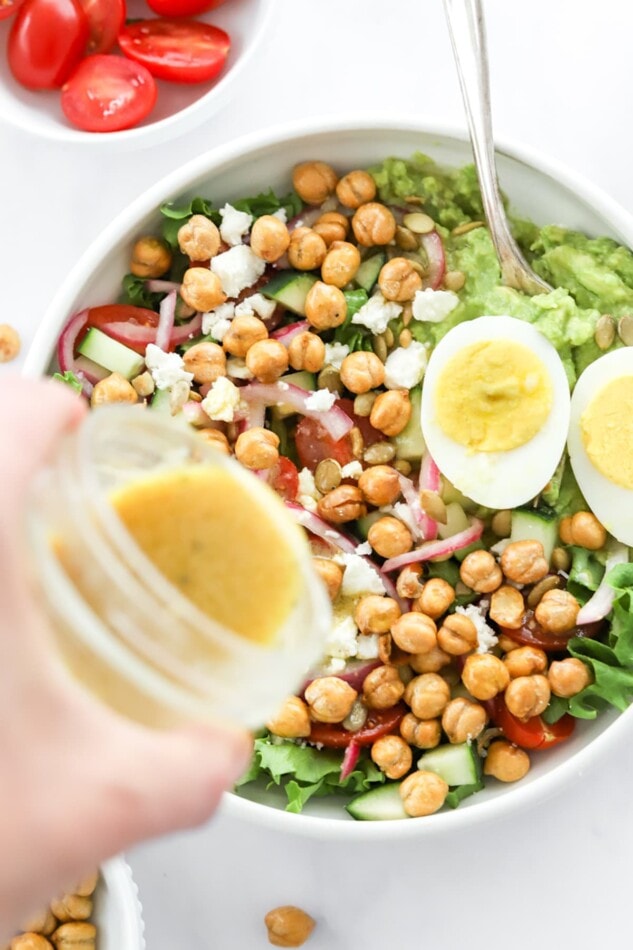 Pouring dressing over top of a mashed avocado bowl.