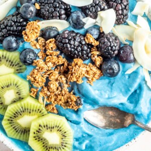 Overhead photo of a blue majik smoothie bowl topped with kiwi, granola, blackberries, blueberries and coconut flakes.