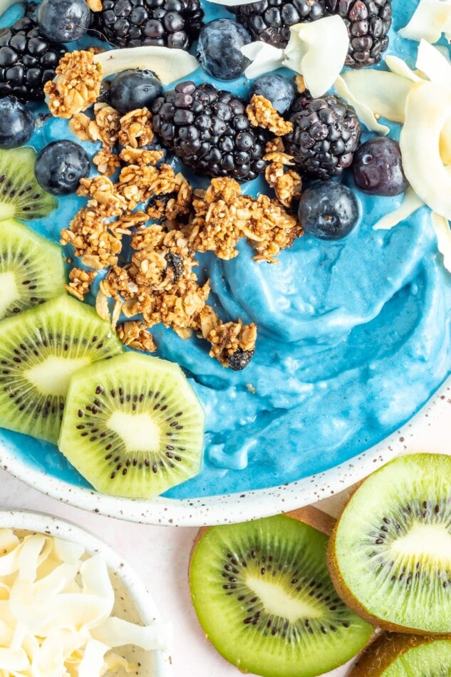 A blue majik smoothie bowl topped with kiwi, blackberries, granola and coconut chips.