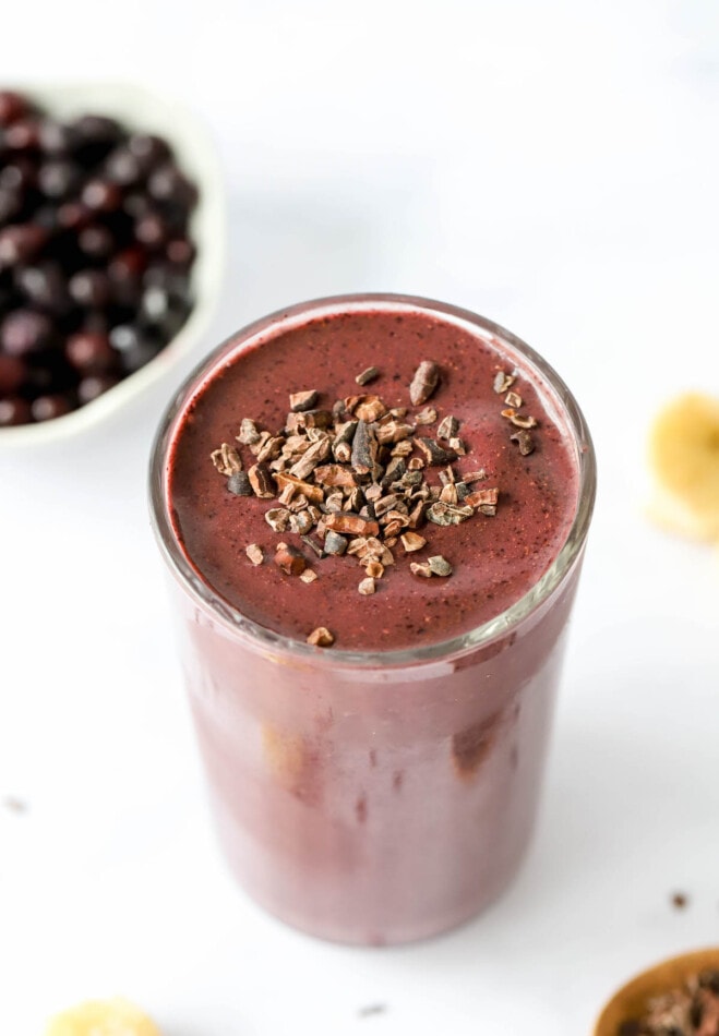 A glass cup filled with cacao smoothie topped with cacao shavings.