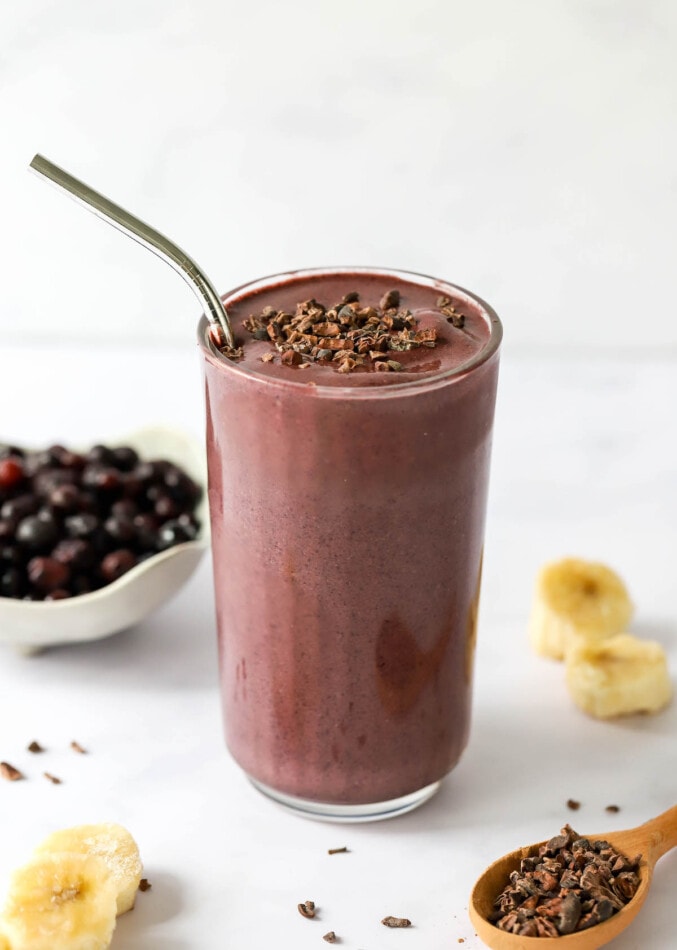 A glass cup containing cacao smoothie. The top has been sprinkled with cacao shavings and a straw sticks out of the glass.