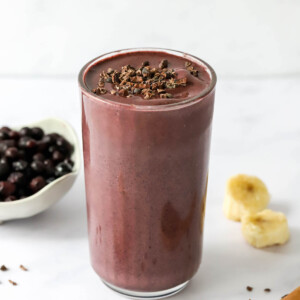 A glass cup filled with cacao smoothie topped with cacao shavings.