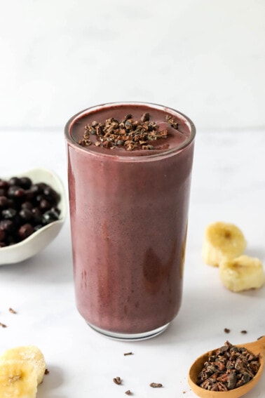 A glass cup filled with cacao smoothie topped with cacao shavings.