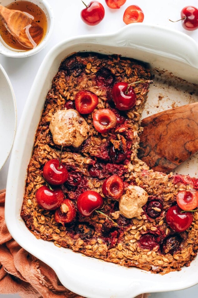 Overhead view of cherry baked oatmeal in a baking dish. A square serving is missing from the dish.