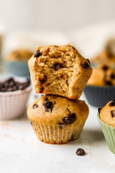 Two chocolate chip yogurt muffins stacked on top of each other. The top muffin has a bite taken out of it.