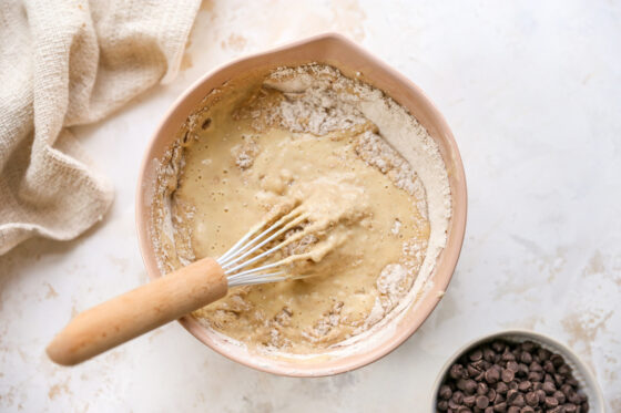 Egg mixture added to dry ingredients in a mixing bowl with a whisk.