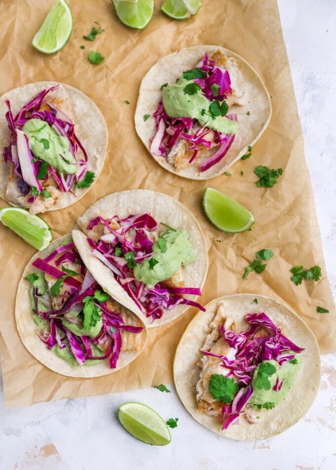 Overhead view of fish tacos scattered across a sheet of parchment paper.