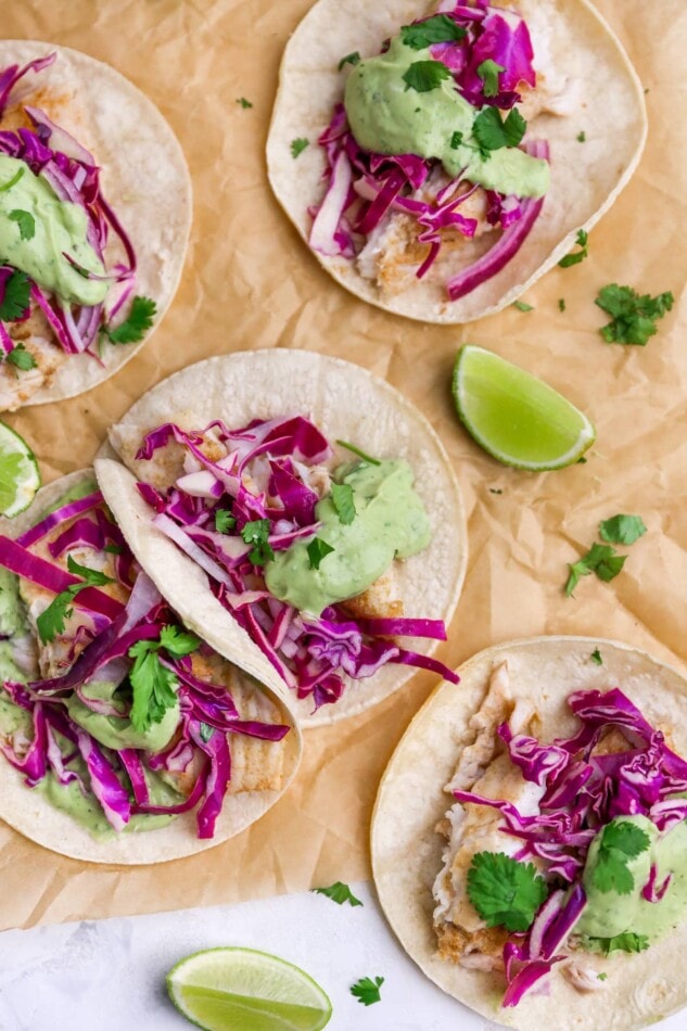 Overhead view of fish tacos scattered across a sheet of parchment paper.