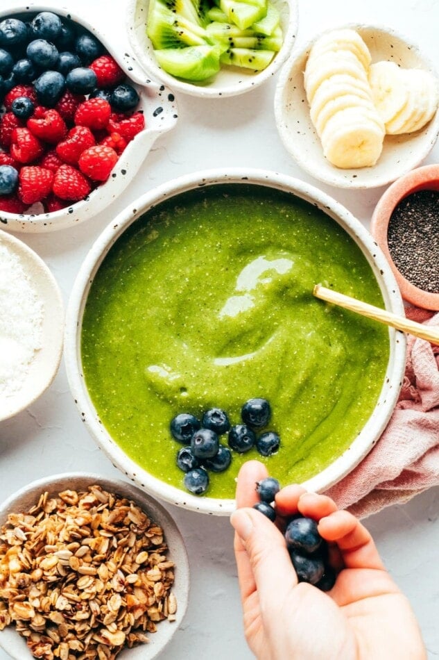 Adding toppings to a green smoothie bowl.