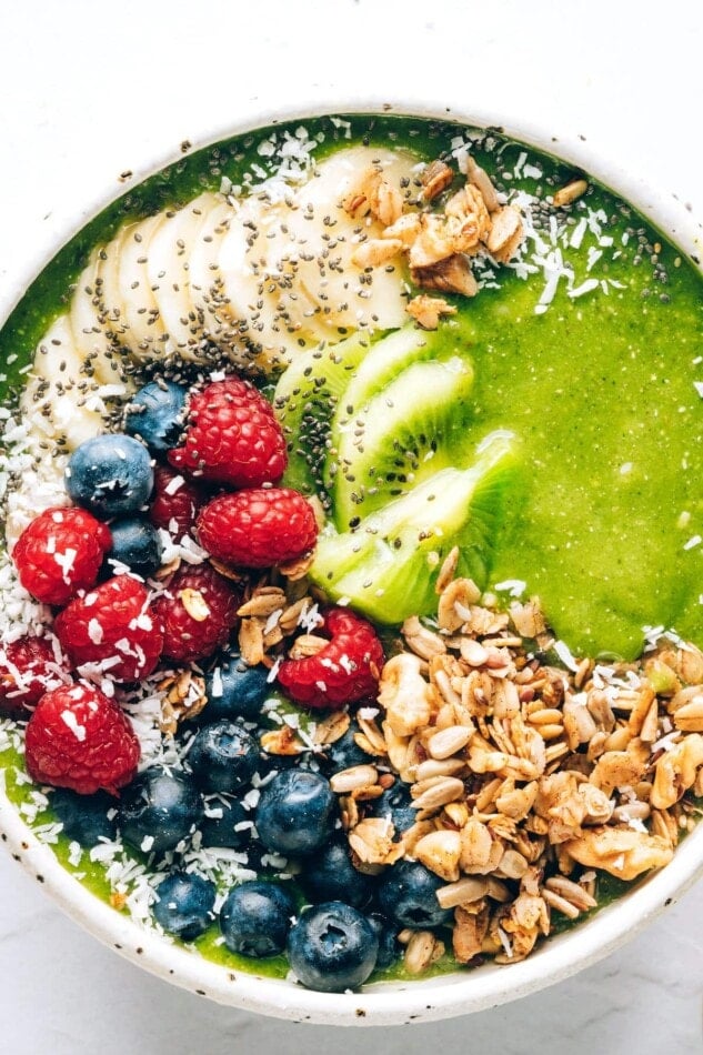 A green smoothie bowl topped with granola, shredded coconut, berries, banana and kiwi.