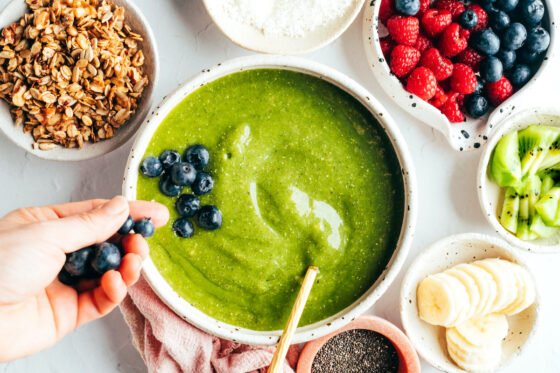 Adding blueberries to a green smoothie bowl.