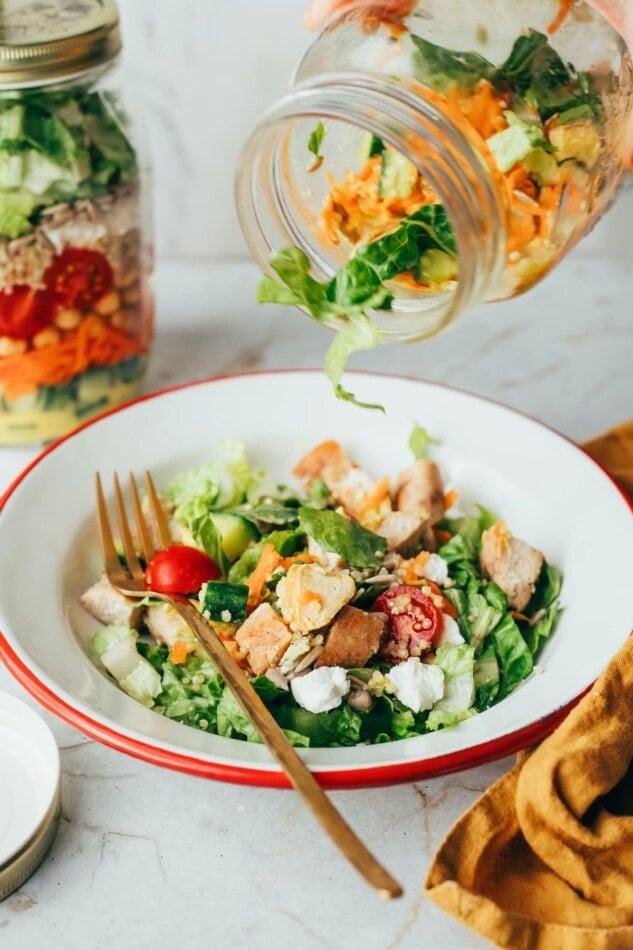 Pouring a mason jar salad into a serving bowl.