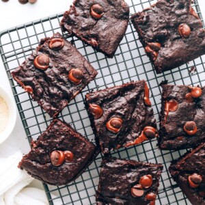 Overhead view of a wire cooling rack with lactation brownies scattered around. A hand is grabbing a brownie from the bottom.