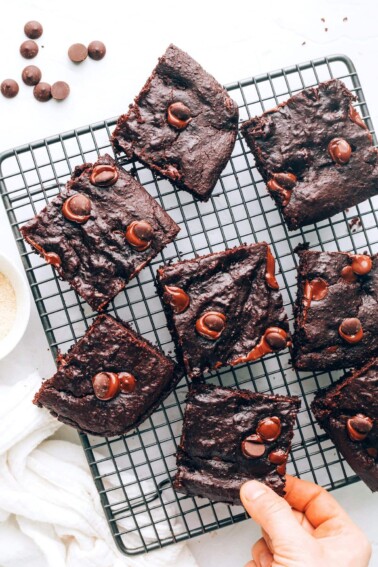 Overhead view of a wire cooling rack with lactation brownies scattered around. A hand is grabbing a brownie from the bottom.