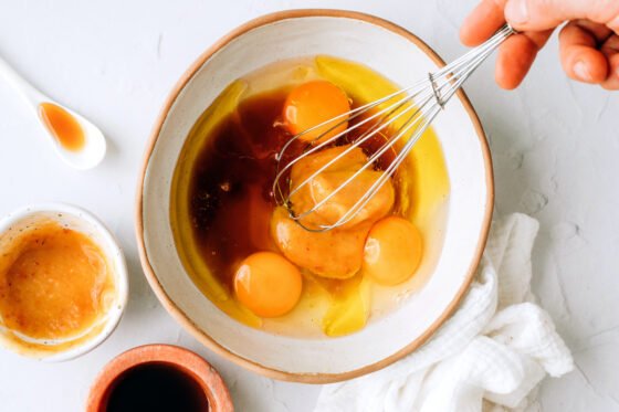 Mixing together eggs, avocado oil, maple syrup, applesauce, and vanilla extract.