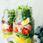 A mason jar containing layers of Nicoise salad ingredients.