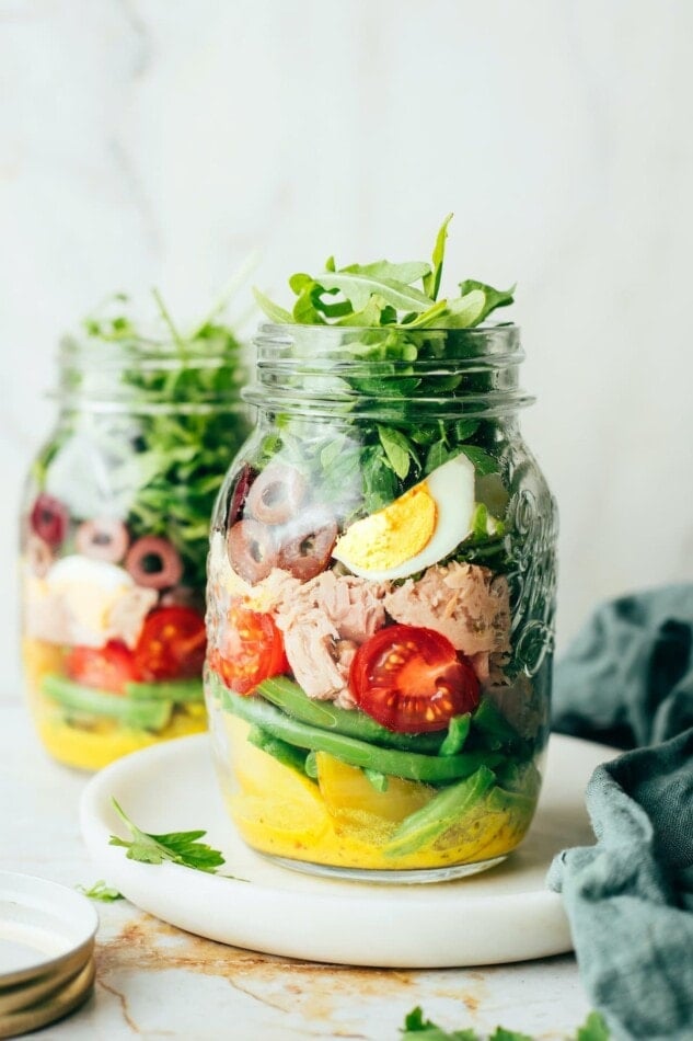 A mason jar containing layers of Nicoise salad ingredients.