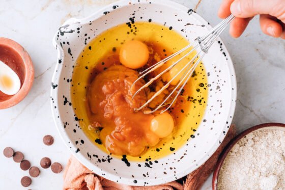 Whisking together eggs, avocado oil, maple syrup, applesauce, and vanilla extract.