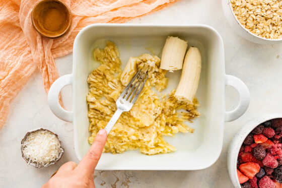 A fork mashing a banana in a square baking dish.